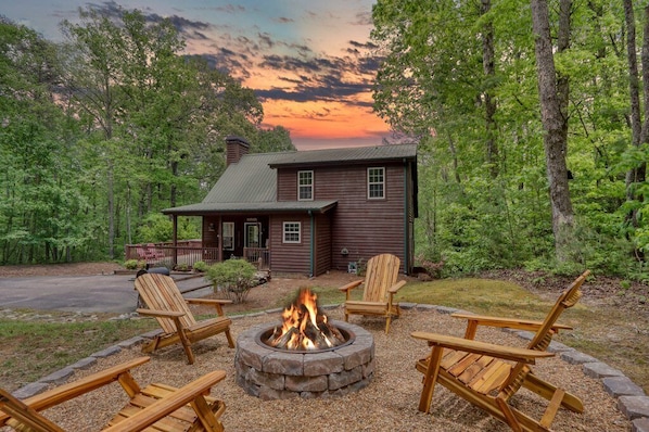 Un chalet rustique avec un foyer et des fauteuils Adirondack, situé dans un cadre forestier.