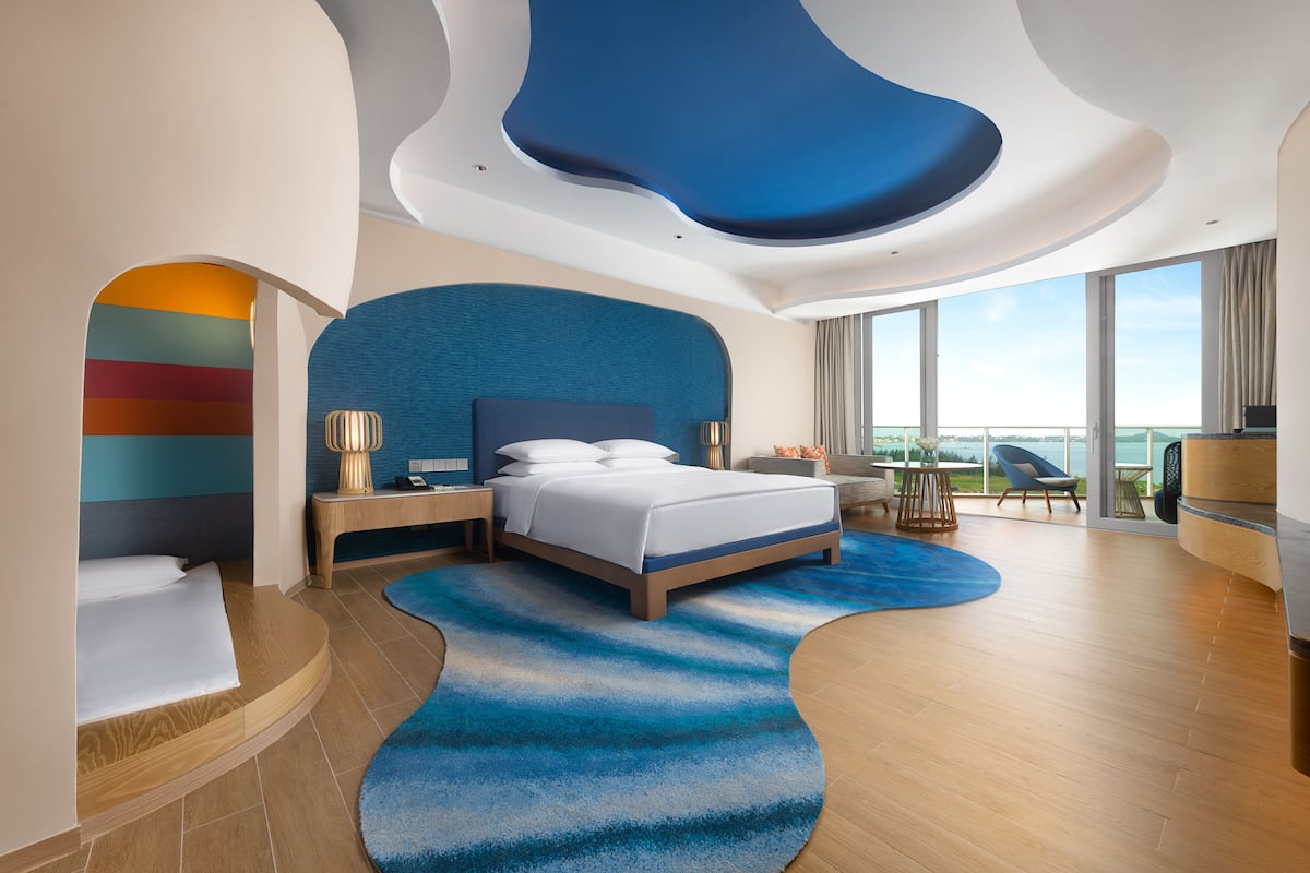 A modern hotel room with a large bed, a desk, and a view of the city.