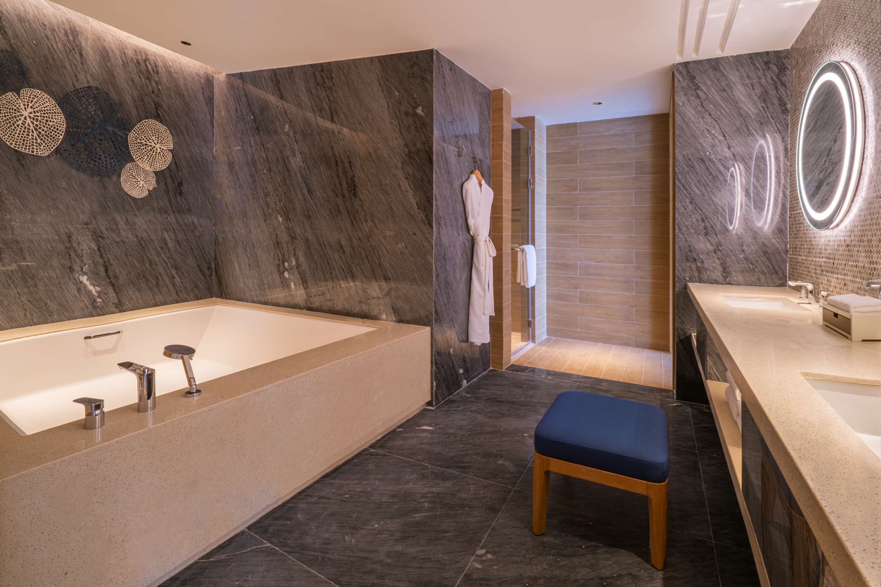 A modern bathroom with a large bathtub, a wooden bench, and a vanity with a mirror.