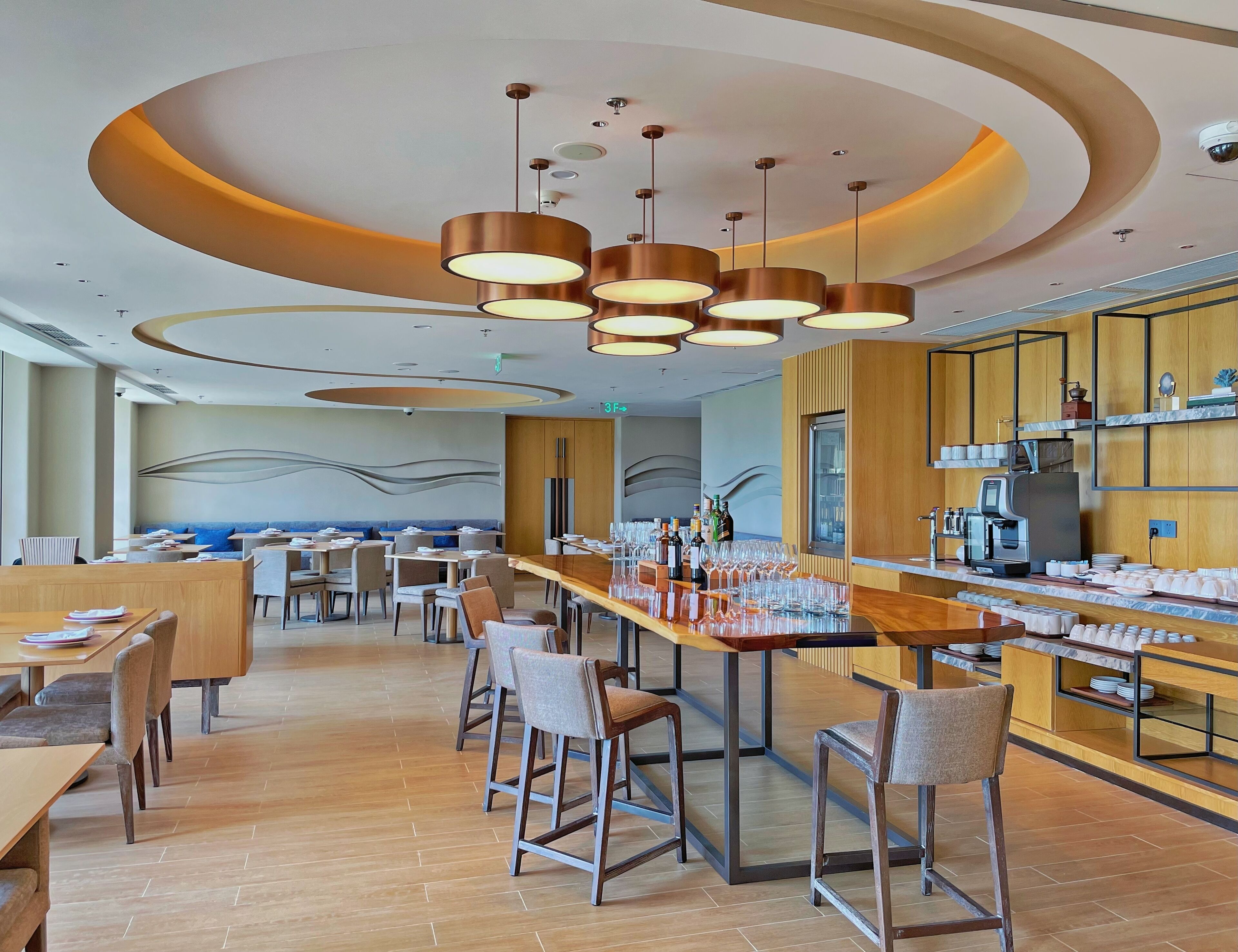 Un restaurante moderno con una barra larga, varias zonas de estar e iluminación contemporánea.