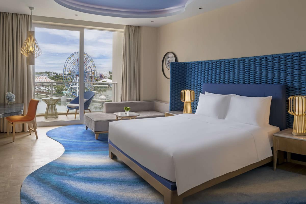 A hotel room with a large bed, a sofa, a dining area, and a view of a Ferris wheel.