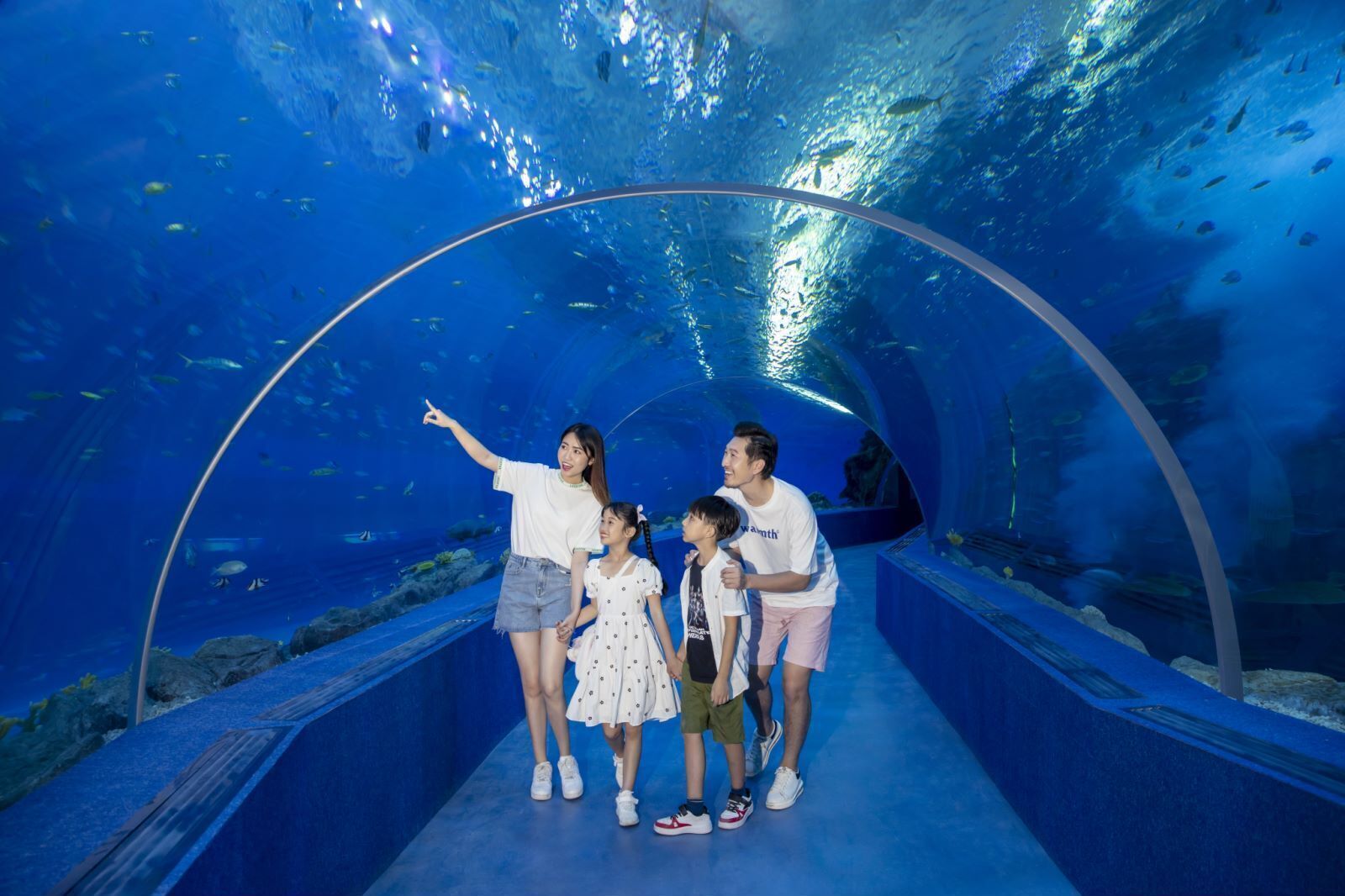 A family inside an underwater tunnel with clear blue water and fish.