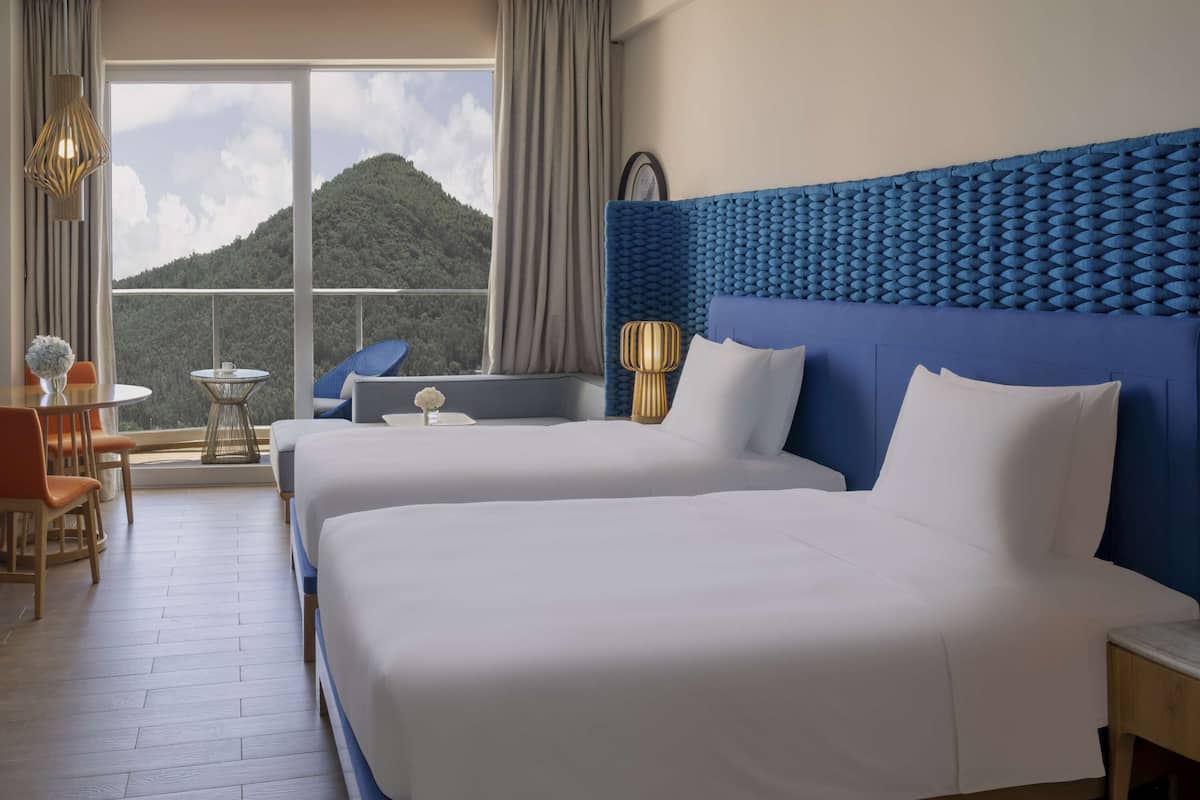 A hotel room with two beds, a view of a mountain, and a balcony with a table and chairs.