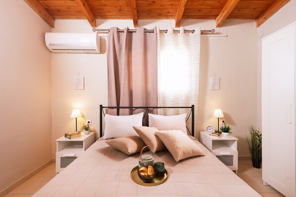 Un dormitorio con una cama, dos mesitas de noche con lámparas, una planta en la mesita y una ventana con cortinas.
