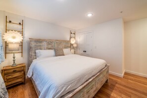 Une chambre à coucher avec un grand lit, une tête de lit en bois, deux tables de chevet avec des lampes et une porte.