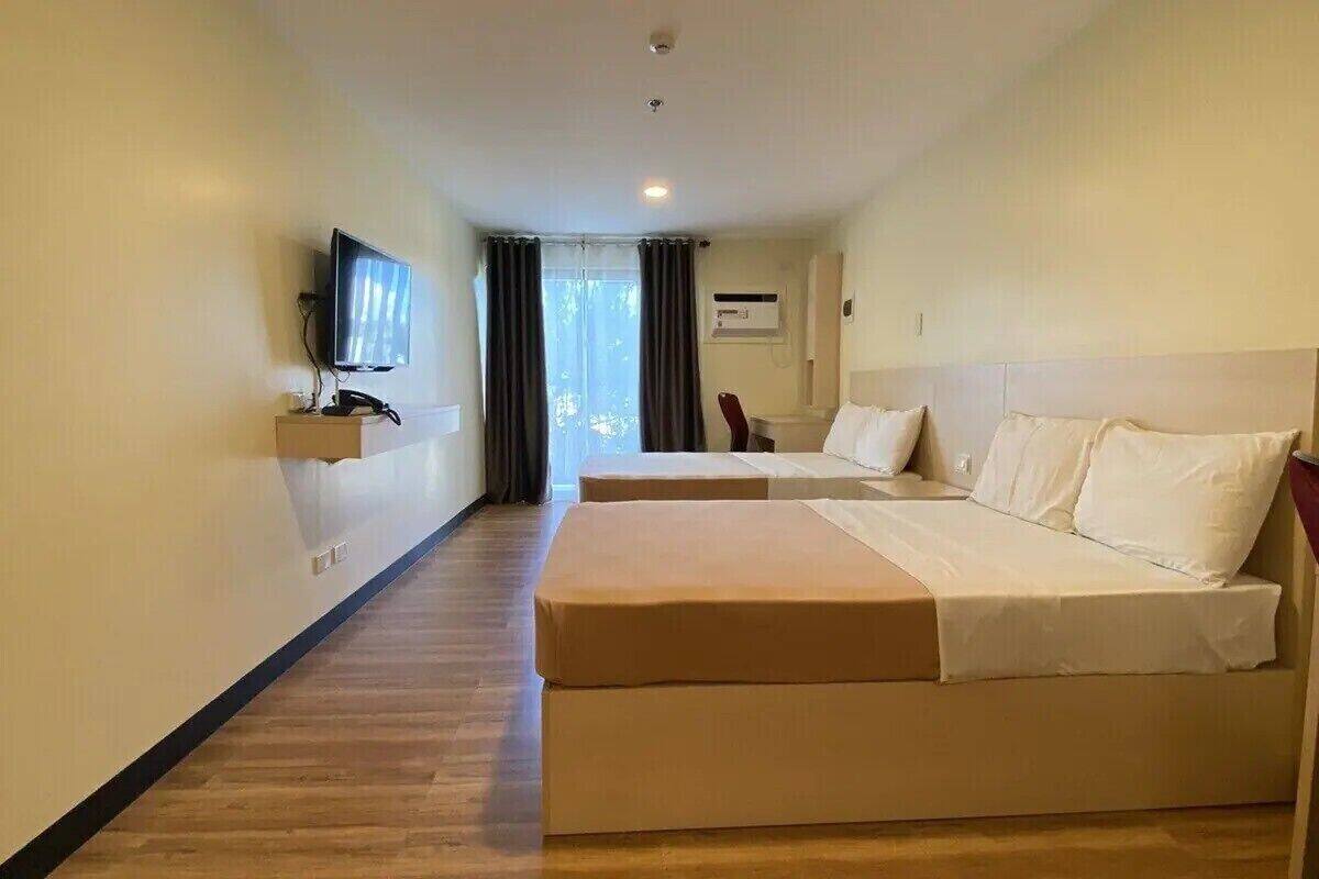 A hotel room with two beds, a television, and a window with curtains.