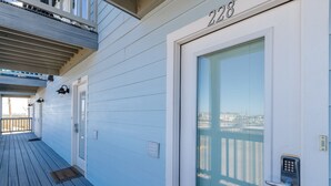 A white door with a numeric keypad lock, a balcony with a railing, and a window with blinds. - Modern Beachside Condo | Ocean Peek Views & Pool (Corpus Christi)
