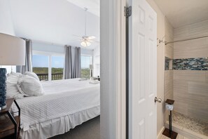 Een slaapkamer met een bed, nachtkastje, lamp, plafondventilator en uitzicht op de omgeving.