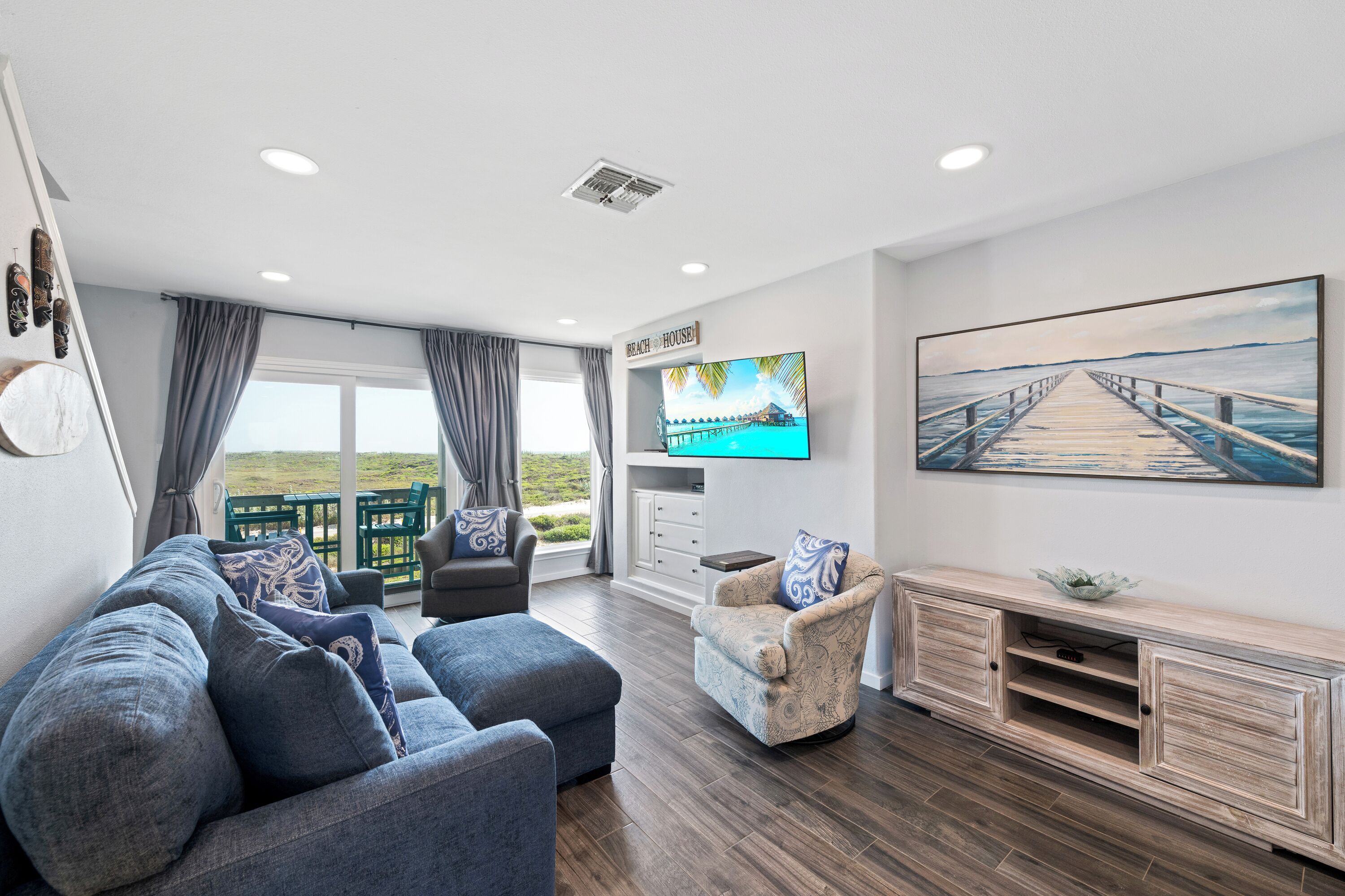 A modern living room with a sofa, armchair, and TV, a wooden cabinet, and a painting of a pier.