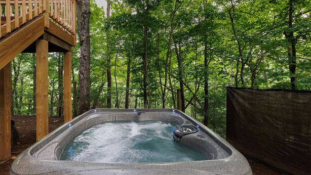 Een hottub in een bebost gebied met een houten terras en een overdekt gedeelte.