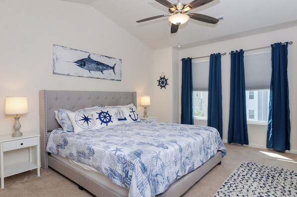 A bedroom with a bed, two bedside tables, a ceiling fan, a window with curtains, and a wall-mounted star decoration.