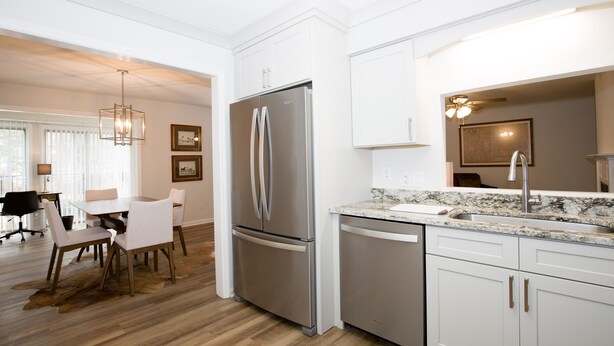A modern kitchen with white cabinetry, a stainless steel refrigerator, a granite countertop, and a dining area with a table and chairs. - 19 F Pinehurst Manor: 1  BR, 1  BA Condominium in Pinehurst, Sleeps 3 (Pinehurst)