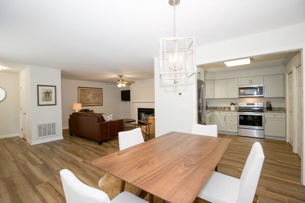 A modern kitchen with white cabinets, stainless steel appliances, and a wooden dining table with white chairs.