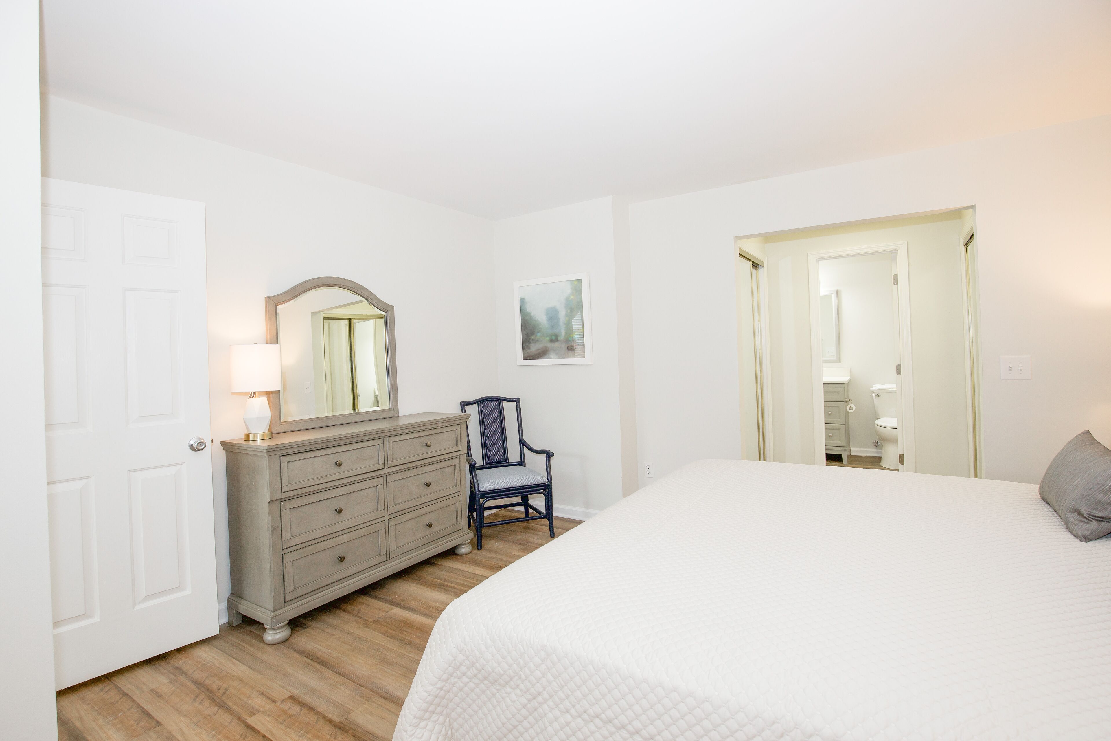 Ein Schlafzimmer mit Bett, Schminktisch, Stuhl und einer Tür zu einem Badezimmer.