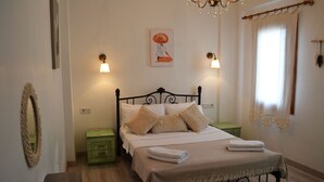 Una cama bien hecha con cabecera, dos mesitas de noche, una lámpara de pared y una ventana con cortinas.
