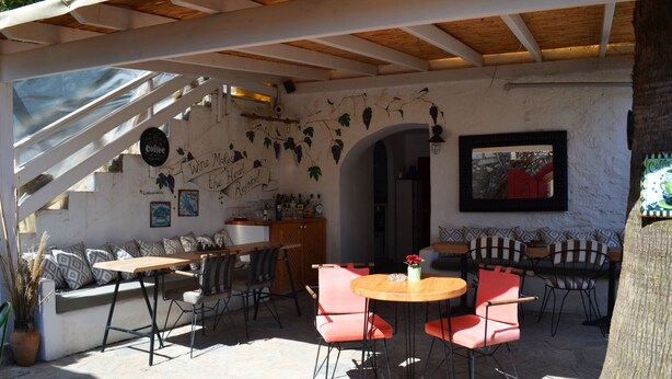 Un área de estar al aire libre con mesas y sillas, techo de madera y una pared decorada con enredaderas de parra.