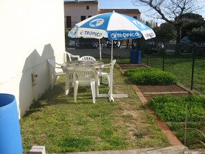 Eine Terrasse mit Tisch und Stühlen, einer blauen Mülltonne und einem Gartenbereich.