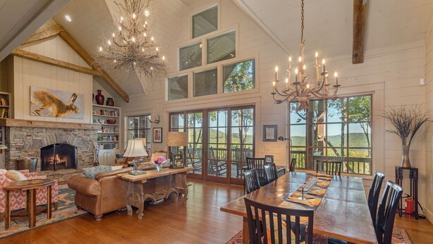 A spacious living room with a fireplace, wooden furniture, and large windows offering a view of the outdoors. - Beautiful custom home in Chinquapin (Glenville)