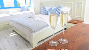 A bedroom with a bed, two champagne glasses on a wooden table, and a window with blue curtains. - Rhodium Hotel (Cesme)