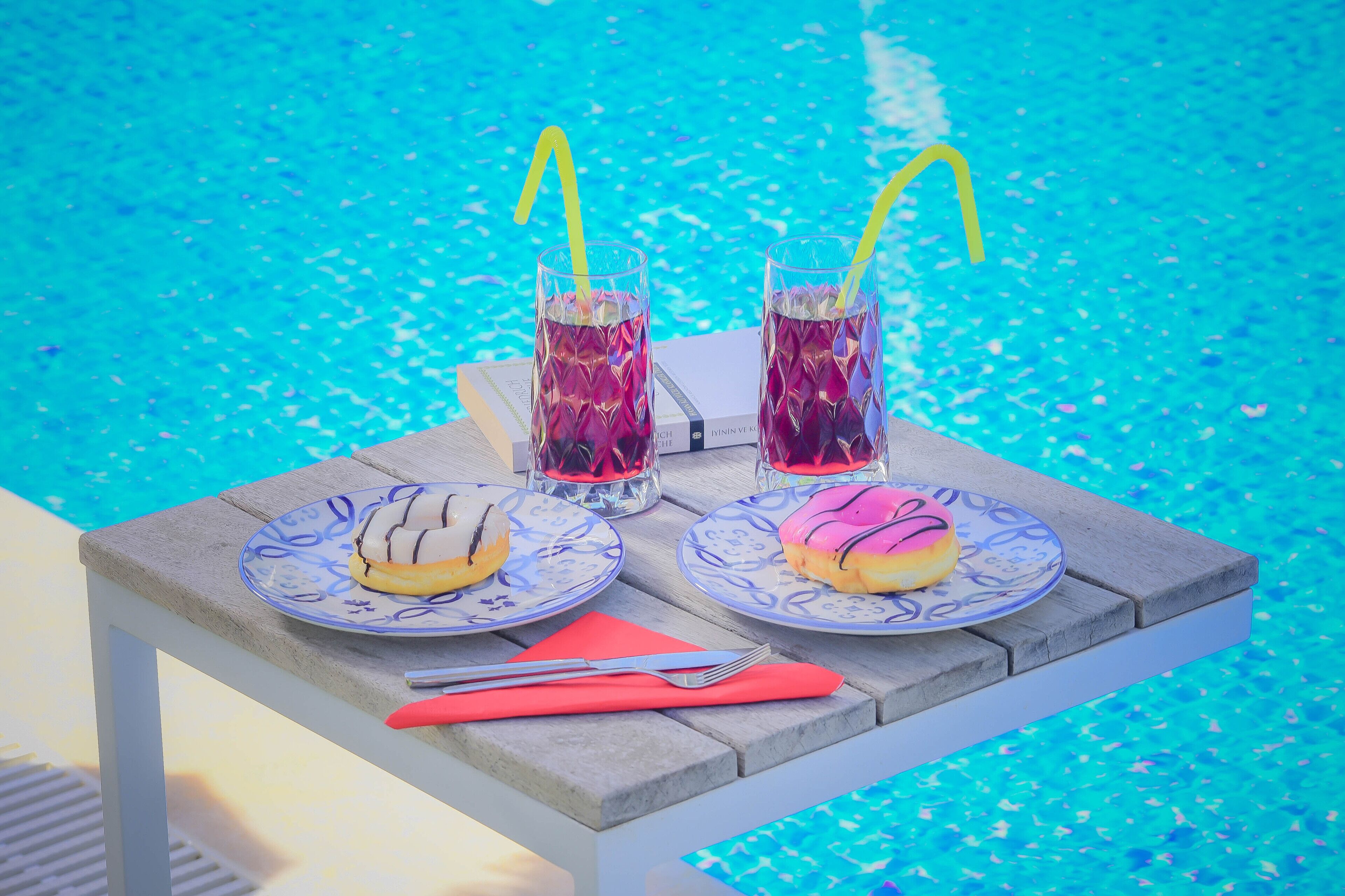 A table with two plates of food, two glasses of iced drinks, and a fork and napkin.