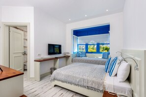 A bedroom with a bed, a TV, a desk, and a window with blue shutters. - Rhodium Hotel (Cesme)