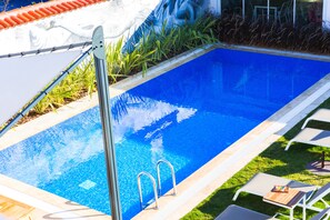 A rectangular swimming pool with clear blue water, surrounded by a tiled deck and a grassy area with lounge chairs. - Rhodium Hotel (Cesme)