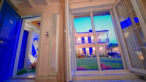 A modern building with a glass entrance, a blue door labeled '10', and a well-lit outdoor area with a lawn and seating. - Rhodium Hotel (Cesme)