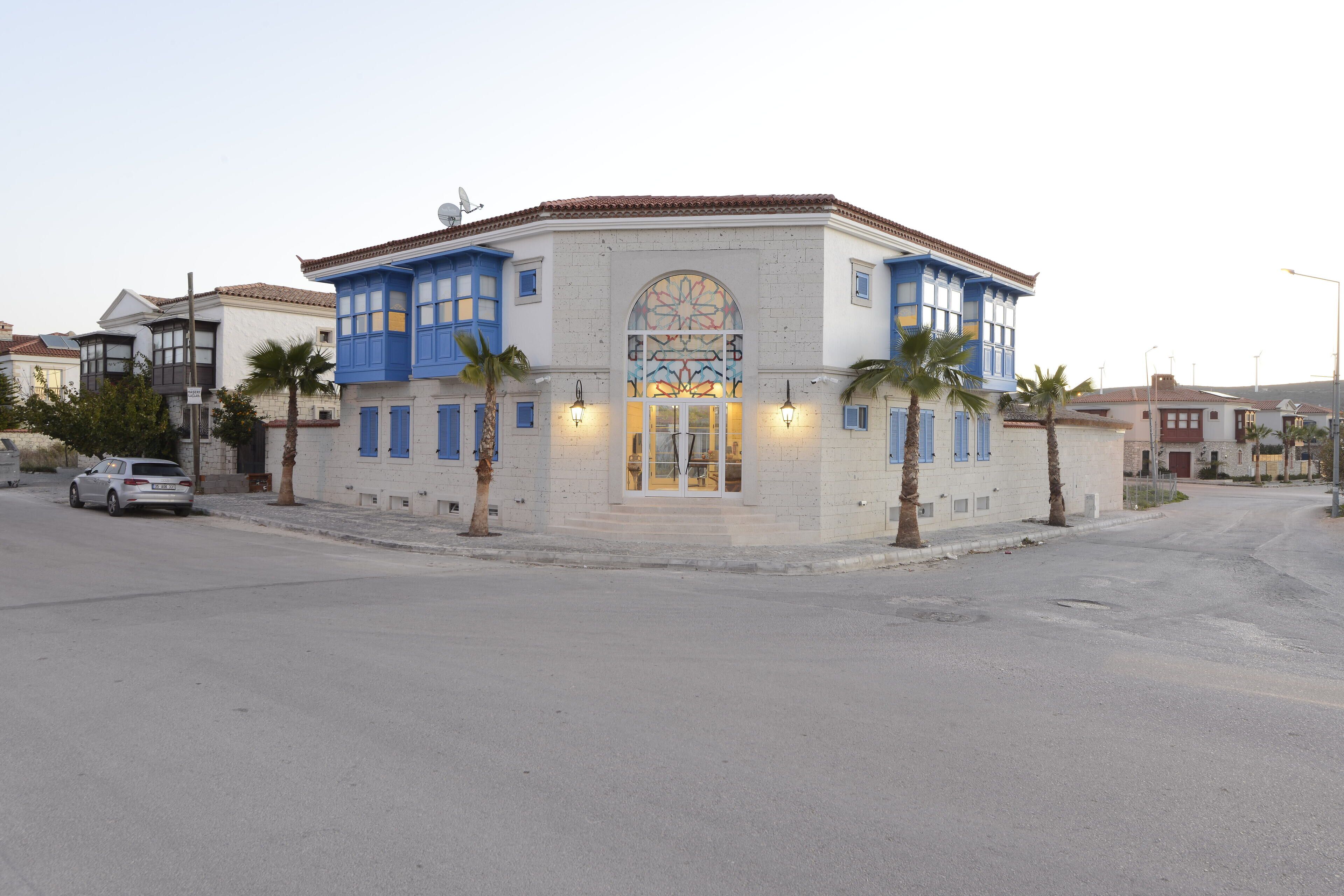 Un edificio con una fachada distintiva azul y blanca, un gran ventanal arqueado y dos palmeras en primer plano.