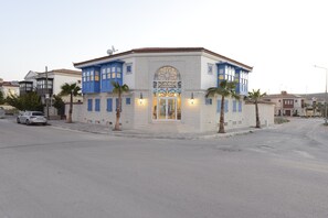 A building with a distinctive blue and white facade, a large arched window, and two palm trees in front. - Rhodium Hotel (Cesme)