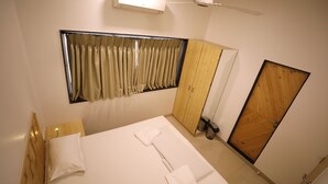 Habitación de hotel con cama, ventana con cortinas, ventilador de techo, equipo de aire acondicionado y armario de madera.