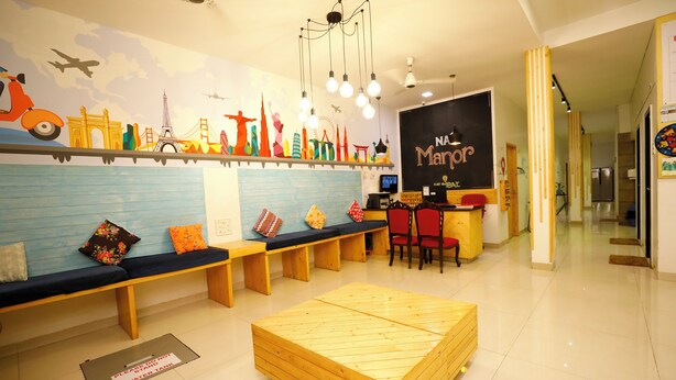 Zona de recepción con disposición de asientos en banco, separador de madera y pared decorada con motivos de viajes.