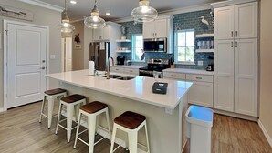 A modern kitchen with a large island, white cabinetry, and pendant lighting. - Deja Blue | Dazzling Townhome, Great Amenities! (Pensacola)