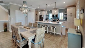 A modern kitchen with a central island, pendant lighting, and a dining area with wicker chairs. - Deja Blue | Dazzling Townhome, Great Amenities! (Pensacola)