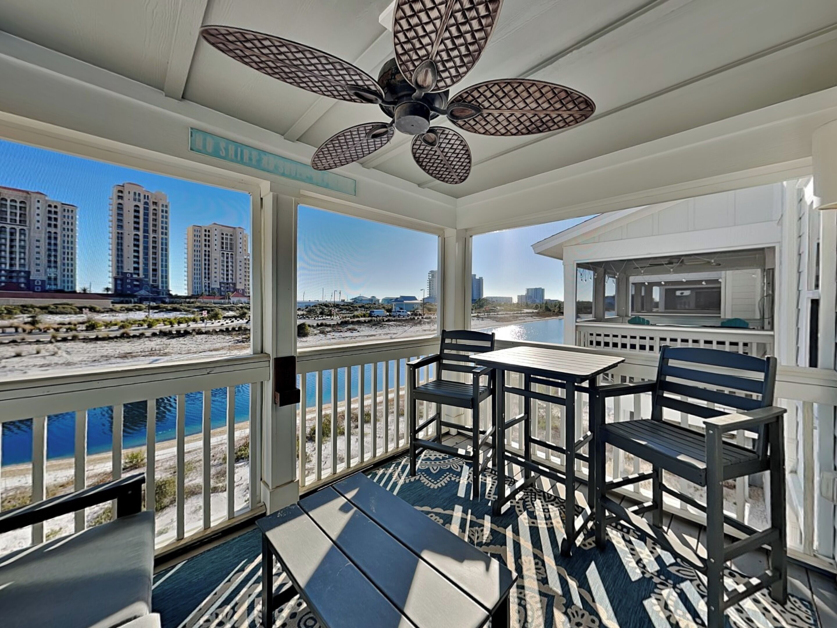 A balcony with a view of the beach and cityscape, a ceiling fan, and a dining area with chairs and a table.