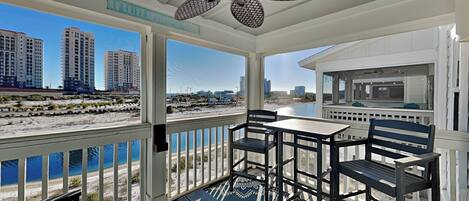 A balcony with a view of the beach and cityscape, a ceiling fan, and a dining area with chairs and a table.