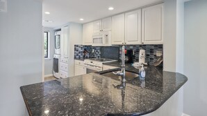 A modern kitchen with white cabinetry, a granite countertop, and stainless steel appliances.