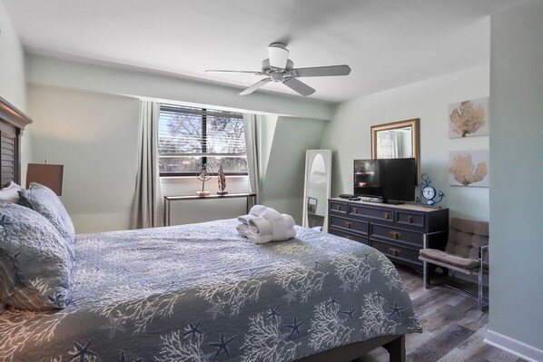 Un dormitorio con cama, cómoda, televisor y ventilador de techo.