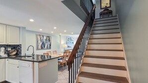 A modern kitchen with white cabinets, a black countertop, and a dining area with wooden chairs.