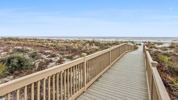 A wooden boardwalk leading to a beach with dunes and sparse vegetation.