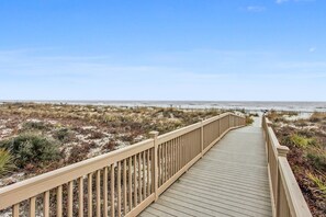 Un camino de madera que lleva a una playa con dunas y vegetación escasa.