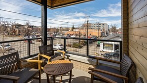A balcony with wooden furniture and a view of a parking lot and buildings. - Rustic Overlook- 30 day rental in the new Merin building in downtown Bozeman! (Bozeman)