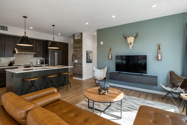 A modern living room with a large brown leather sofa, a wooden coffee table, and a TV mounted on the wall.