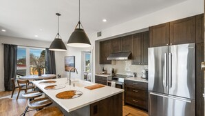 A modern kitchen with dark wooden cabinets, stainless steel appliances, and a central island with stools. - Rustic Overlook- 30 day rental in the new Merin building in downtown Bozeman! (Bozeman)