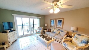 A living room with a sofa, armchairs, a coffee table, a TV, and a balcony with a view.