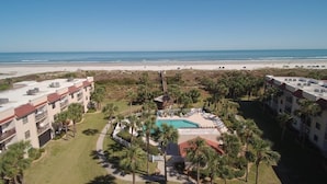 A resort with a central pool, surrounded by palm trees and a beach view.