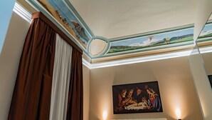 Una habitación con un mural en el techo, un cuadro y una ventana con cortinas.