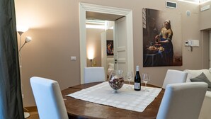 Un comedor con una mesa redonda, sillas blancas, un florero con flores, botellas de vino y copas.