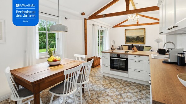 A modern kitchen with white cabinetry, a wooden dining table, and a fruit bowl. - My deer House - Green retreat for the whole family (Wörthsee)