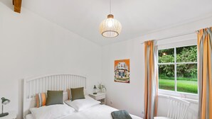 Ein Schlafzimmer mit Bett, Sessel, Nachttisch, Lampe, Fenster mit Vorhängen und einer Pendelleuchte.