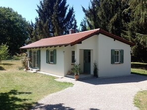 A small, single-story house with a red-tiled roof, white walls, and green shutters. It has a gravel driveway and is surrounded by trees. - My deer House - Green retreat for the whole family (Wörthsee)
